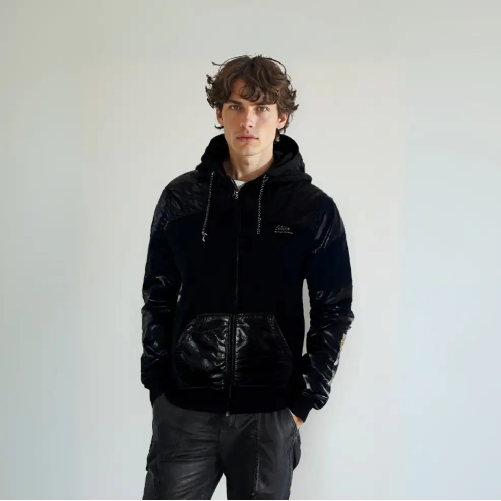 Modelo joven con sudadera negra de cremallera frontal, resaltando el diseño híbrido con paneles de material brillante en hombros, mangas y bolsillos, de la colección exclusiva de Dubrovnik