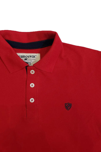 Niño sonriendo con un polo de manga corta en color rojo vibrante con detalles en azul marino en el cuello, combinado con bermudas beige, de la marca Dubrovnik Kids