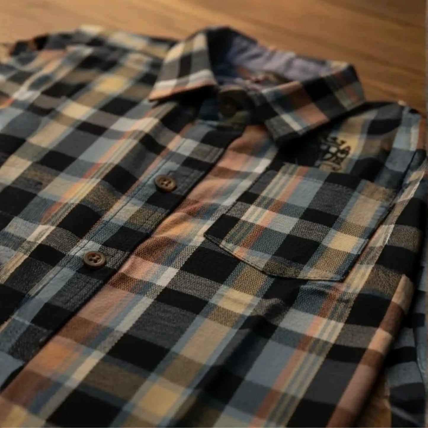 Vista en ángulo de camisa de cuadros para niño en colores gris, azul y naranja con enfoque en el bolsillo y cuello