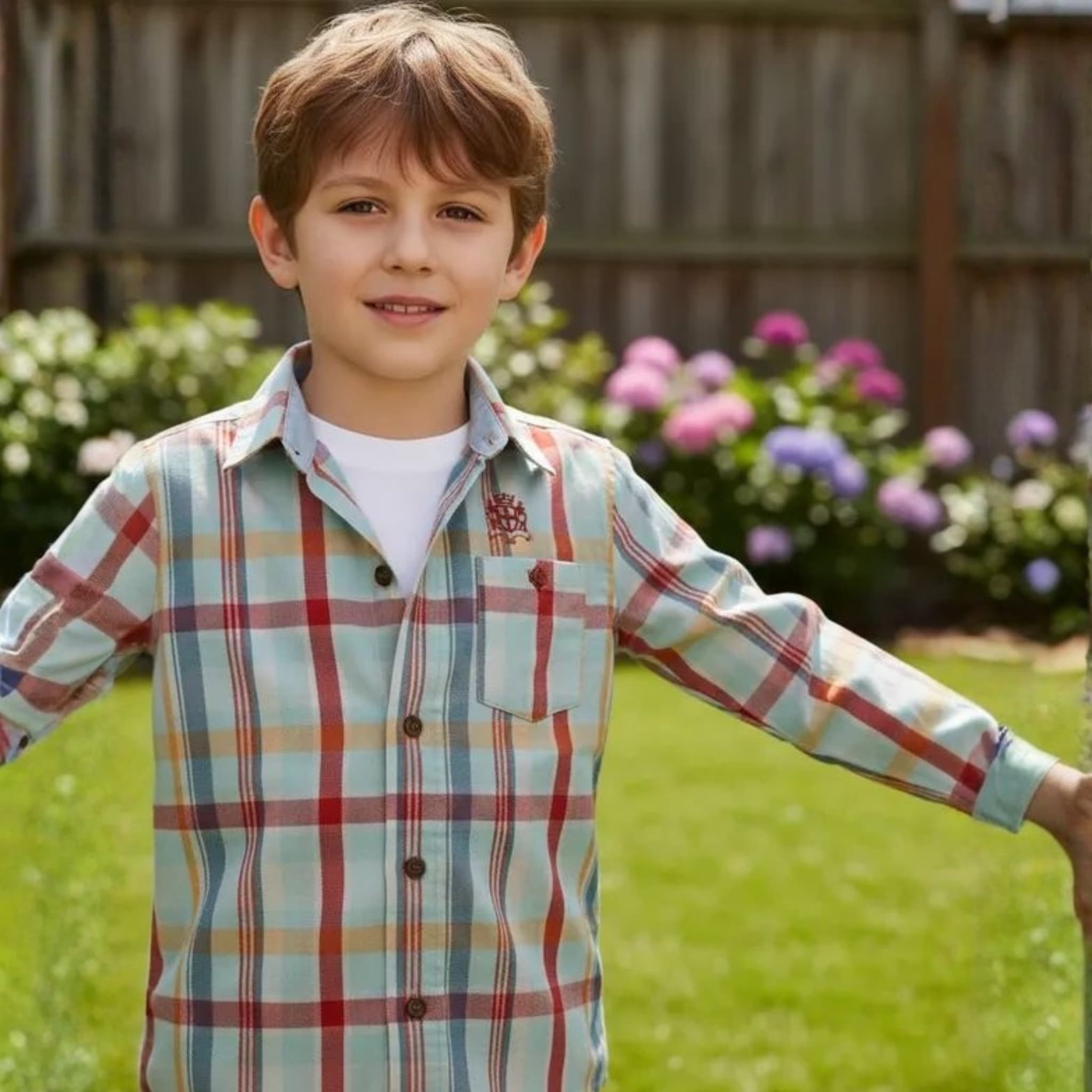 Niño sonriendo con camisa de cuadros multicolor en tonos azul y beige sobre fondo de jardín