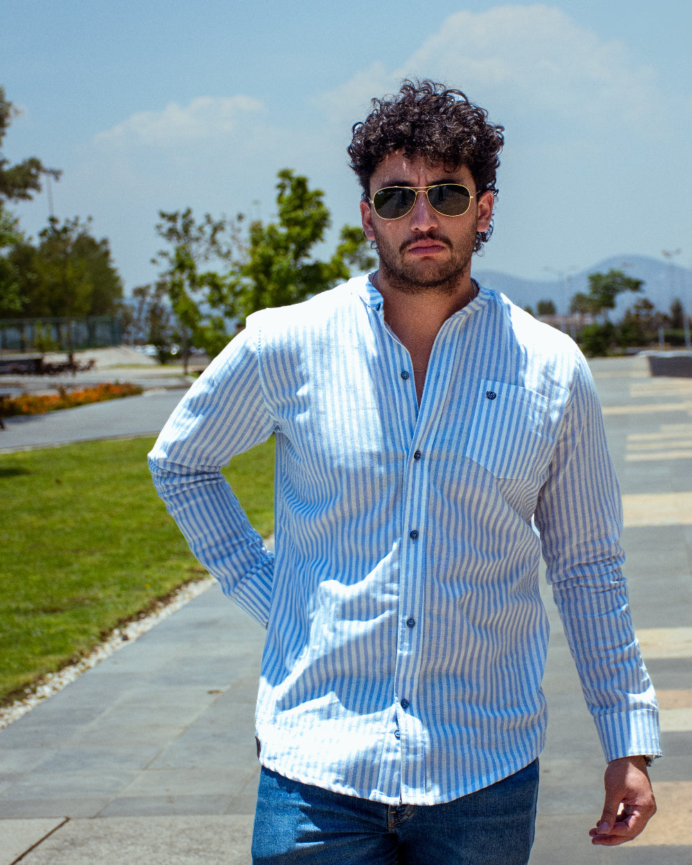 Hombre con gafas de sol posando en el exterior con camisa de cuello mao a rayas blancas y celestes de la marca Dubrovnik