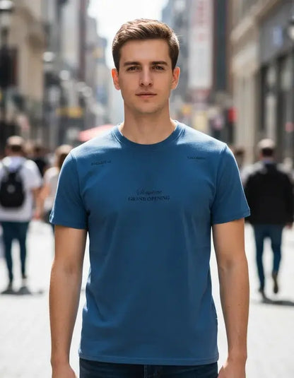 Hombre posando en una calle concurrida con camiseta color azul petróleo de la colección Showtime de Dubrovnik, destacando el texto "Grand Opening" en el pecho y detalles en los hombros