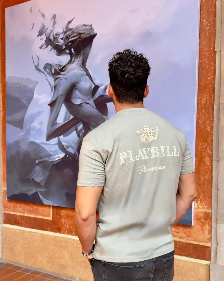 Vista trasera de hombre con camiseta color gris piedra de la marca Dubrovnik, destacando el gráfico de una corona dorada y los textos "PLAYBILL" y "Showtime" en blanco