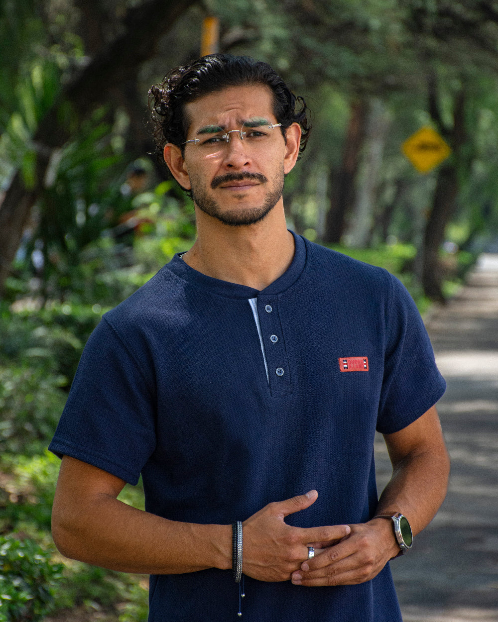 Hombre con gafas luciendo una camiseta tipo Henley azul marino con textura, botones frontales y detalle de etiqueta roja en el pecho