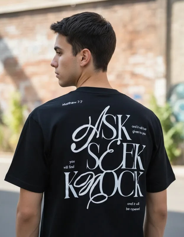 Vista trasera de hombre con camiseta negra de manga corta, destacando el diseño tipográfico ASK SEEK KNOCK