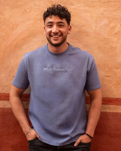 Hombre sonriente con camiseta texturizada en color azul lavanda y gráfico frontal "Trendy Business Club" de la marca Dubrovnik