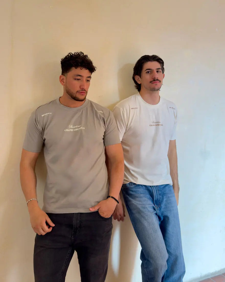 os hombres posando con camisetas de la colección Showtime de Dubrovnik; uno viste el modelo en color gris piedra y otro en color blanco hueso, ambas con el texto "Showtime Grand Opening" en el pecho