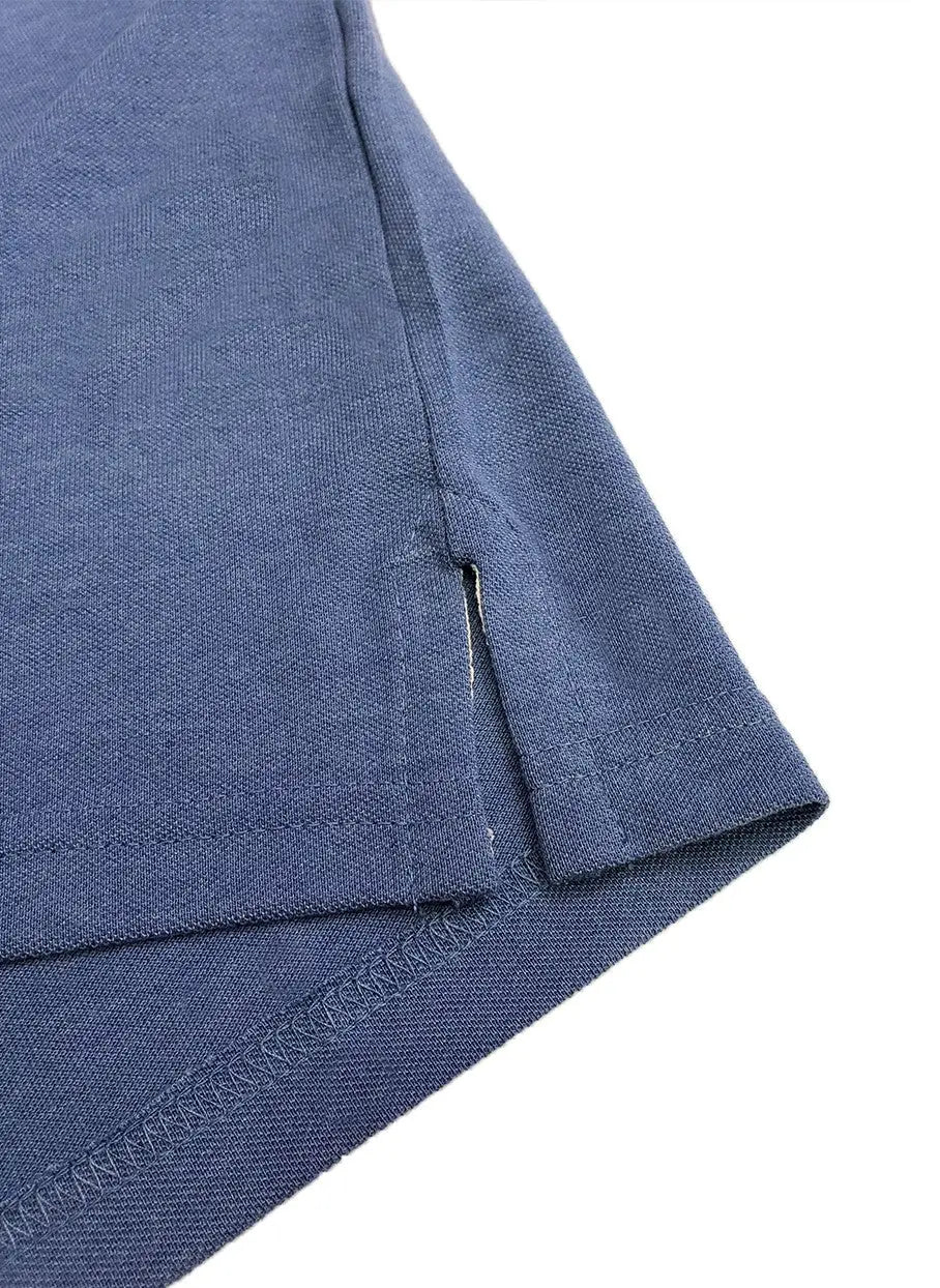 Primer plano del acabado inferior de un polo Dubrovnik azul jaspe, resaltando la aletilla lateral reforzada y la calidad de la doble costura en el bajo