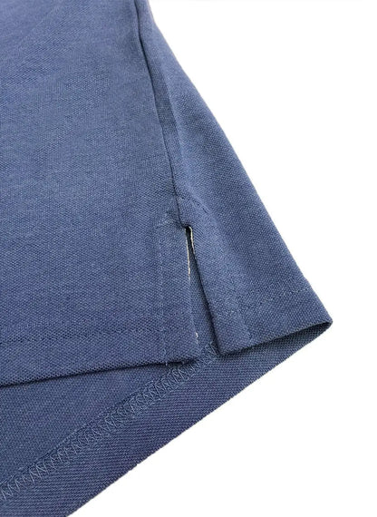 Primer plano del acabado inferior de un polo Dubrovnik azul jaspe, resaltando la aletilla lateral reforzada y la calidad de la doble costura en el bajo