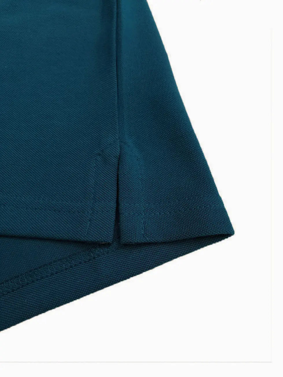 Primer plano del detalle de la costura y abertura lateral de un polo infantil en color azul petróleo, resaltando la textura del tejido piqué de alta calidad de la marca Dubrovnik