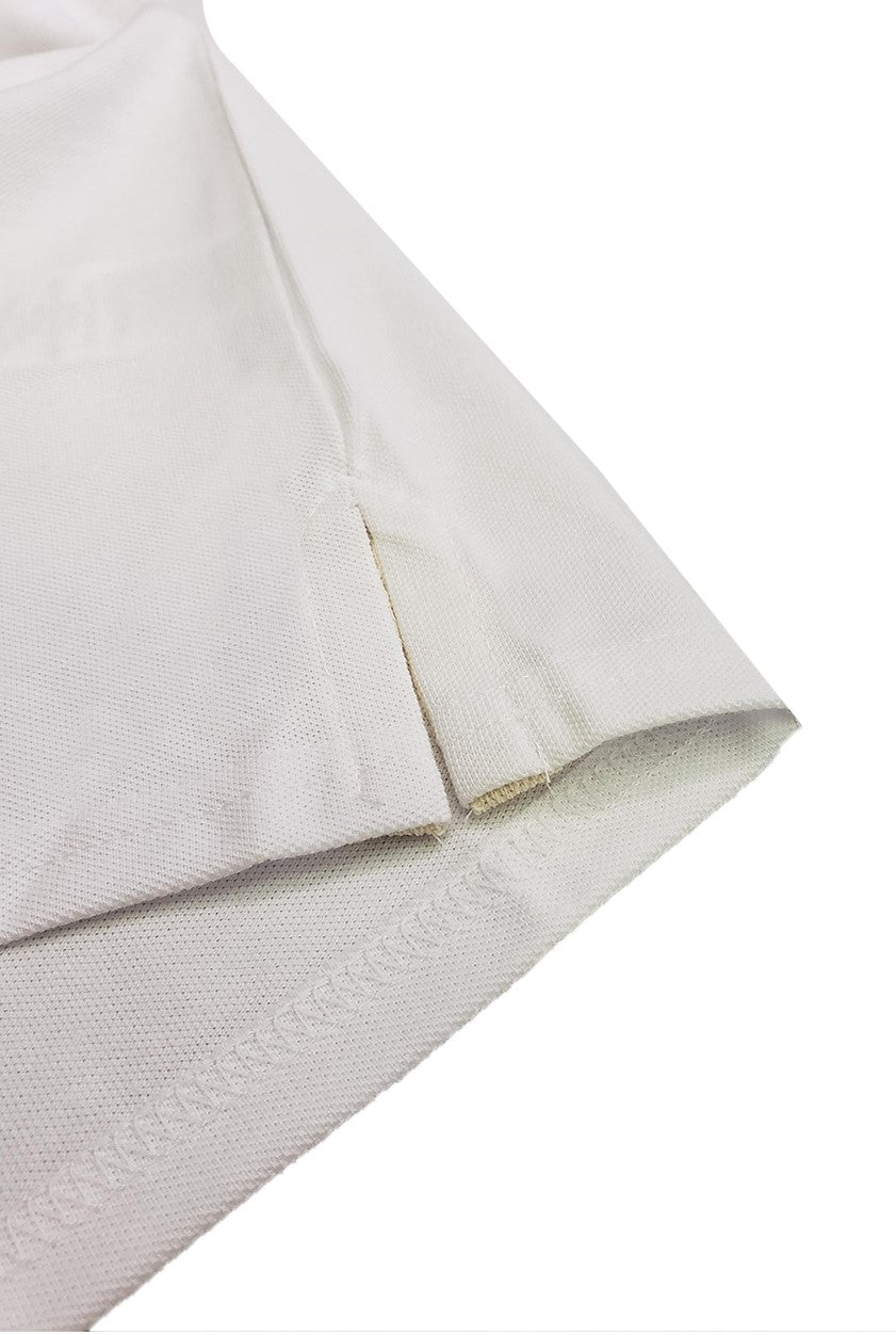 Primer plano del detalle de la costura y la abertura lateral inferior de un polo infantil en color blanco, resaltando la textura del tejido piqué de alta calidad de la marca Dubrovnik
