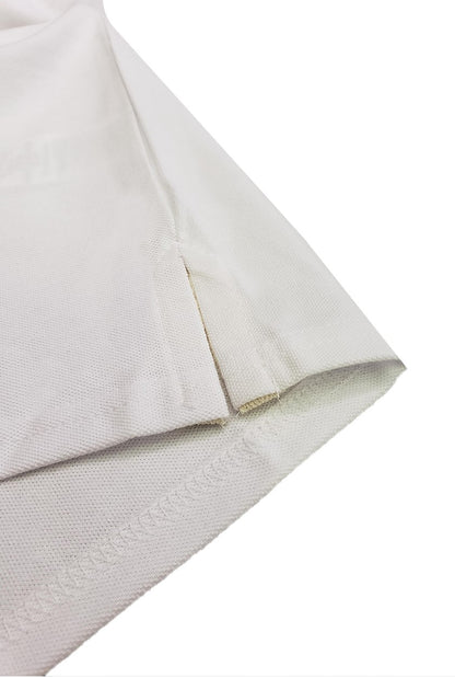 Primer plano del detalle de la costura y la abertura lateral inferior de un polo infantil en color blanco, resaltando la textura del tejido piqué de alta calidad de la marca Dubrovnik