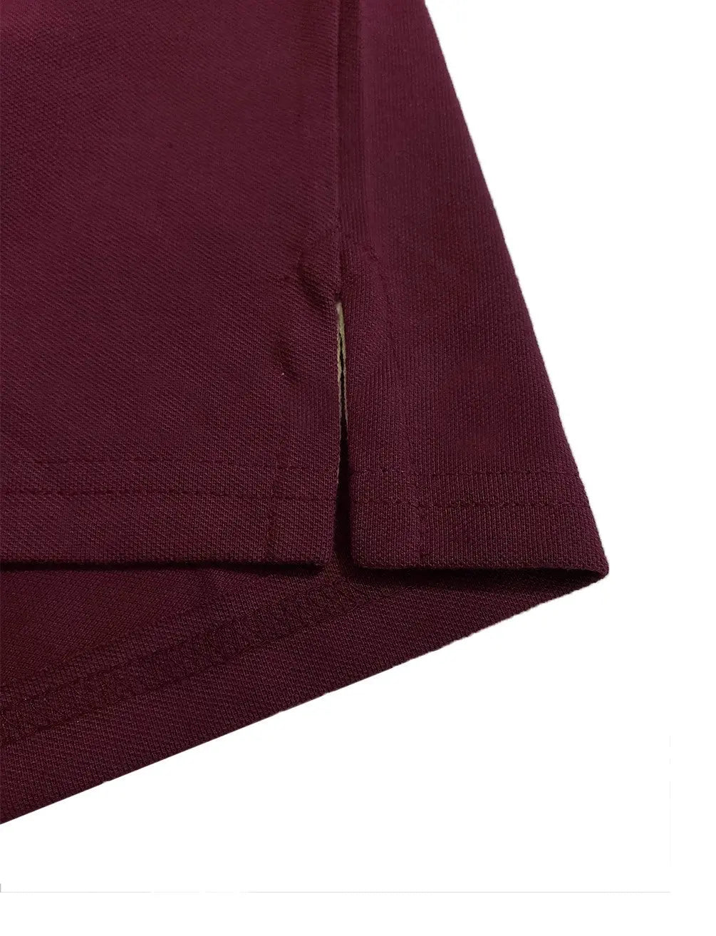 Primer plano del detalle de la costura y abertura lateral inferior de un polo en color ciruela, mostrando la terminación y textura del tejido de la marca Dubrovnik.