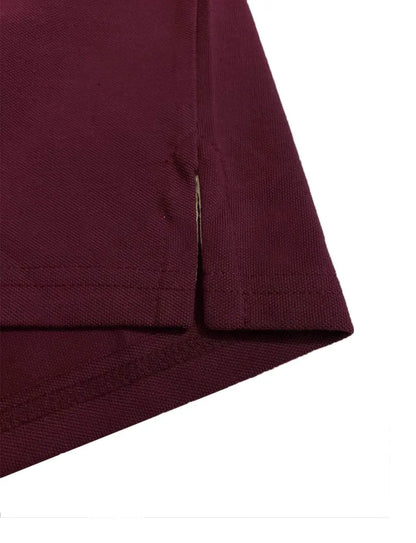 Primer plano del detalle de la costura y abertura lateral inferior de un polo en color ciruela, mostrando la terminación y textura del tejido de la marca Dubrovnik.