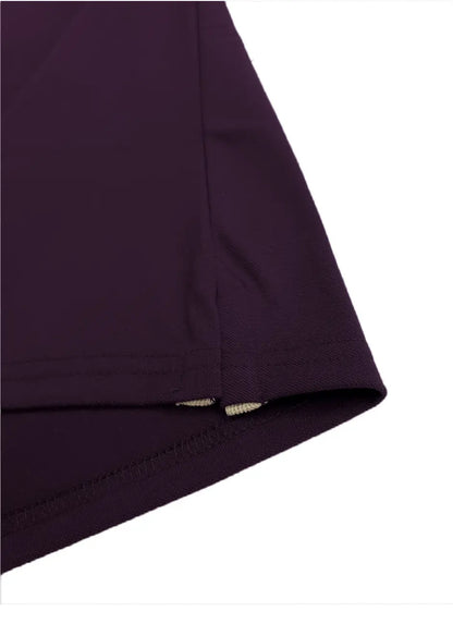 Primer plano del acabado inferior de un polo Dubrovnik color morado imperial profundo, mostrando la aletilla lateral reforzada con cinta interna en gris claro sobre tejido piqué