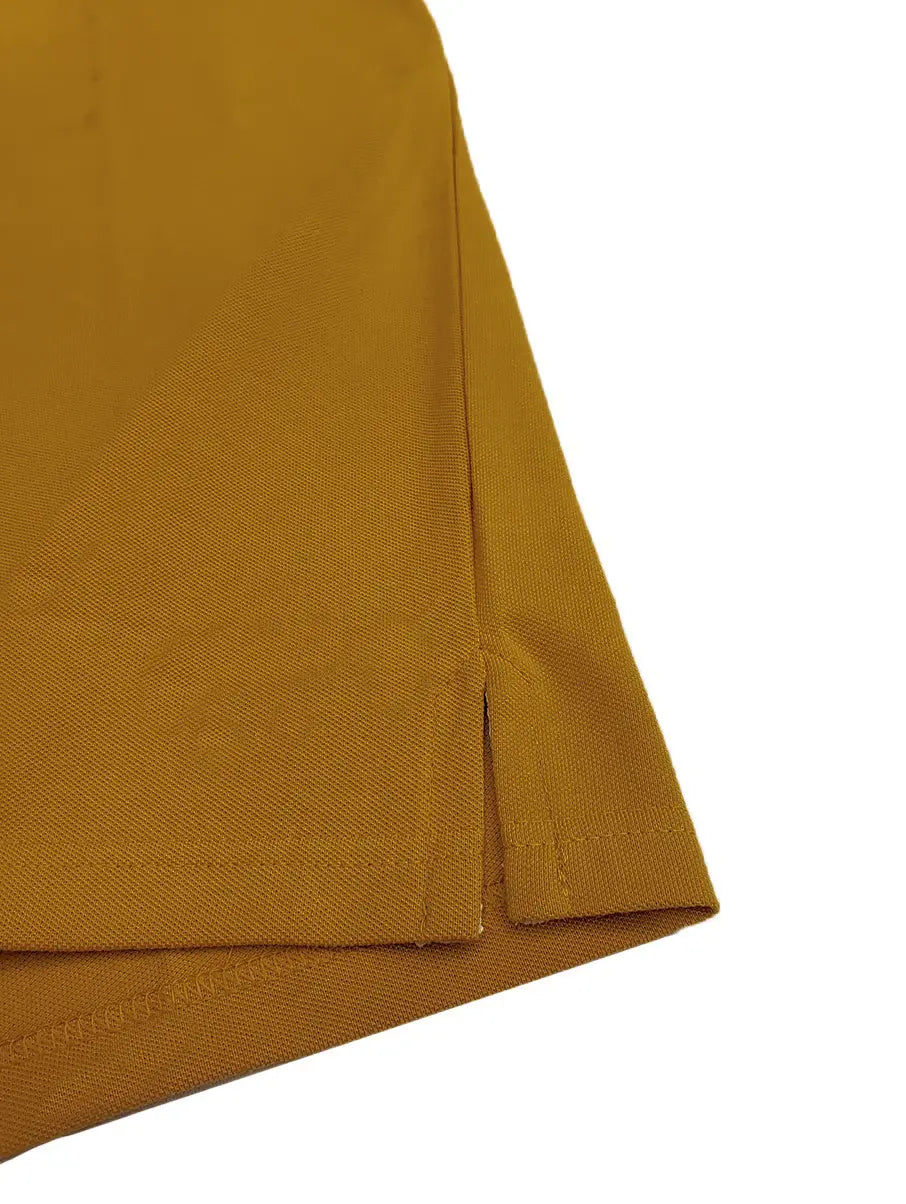 Primer plano del acabado inferior de un polo Dubrovnik color mostaza, mostrando la aletilla lateral (side vent) con costuras reforzadas de alta precisión sobre tejido piqué