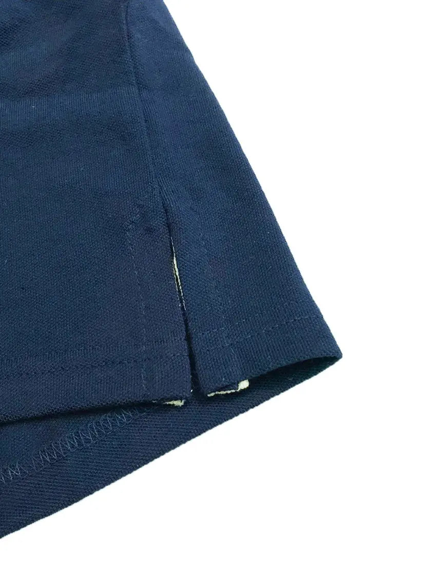 Primer plano del acabado inferior de un polo Dubrovnik azul marino, mostrando la aletilla lateral reforzada, la costura de seguridad y la textura de la mezcla 50/50 algodón-poliéster