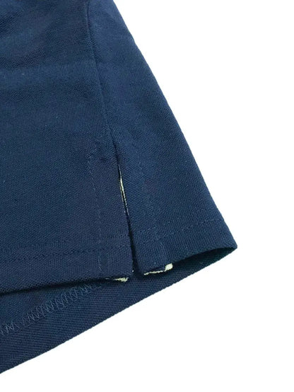Primer plano del acabado inferior de un polo Dubrovnik azul marino, mostrando la aletilla lateral reforzada, la costura de seguridad y la textura de la mezcla 50/50 algodón-poliéster