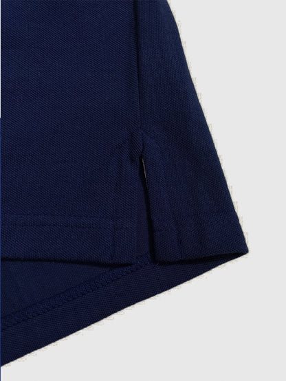 Primer plano del acabado inferior de un polo Dubrovnik azul marino, resaltando la aletilla lateral con refuerzo de seguridad y la precisión de la doble costura en tejido piqué premium