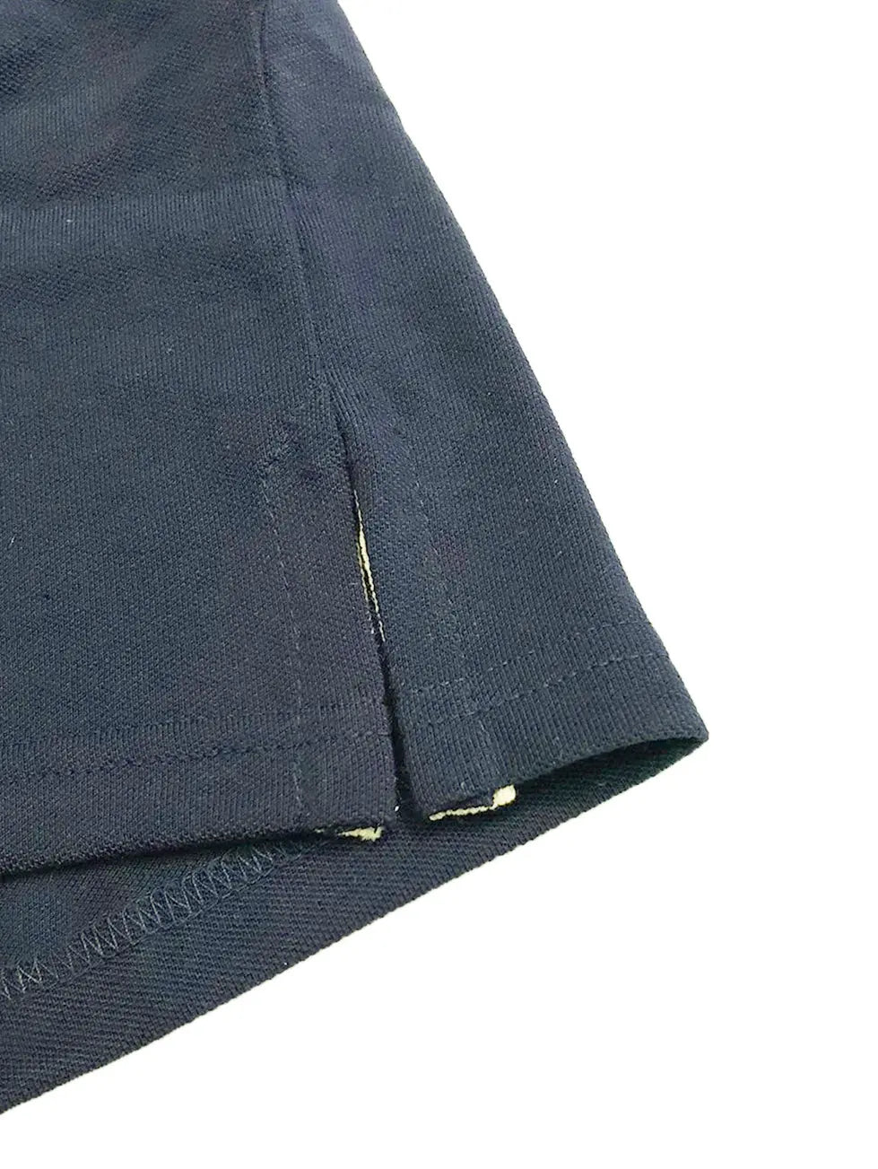 Primer plano del acabado inferior de un polo Dubrovnik color azul petróleo, mostrando la abertura lateral con cinta de refuerzo interna en tono contraste claro