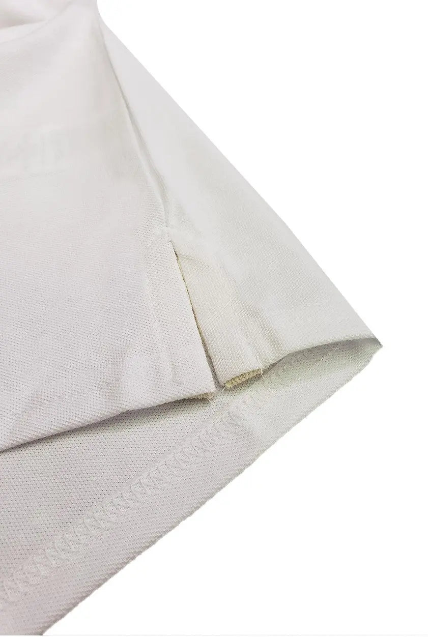 Primer plano del acabado inferior de un polo Dubrovnik color blanco, destacando la abertura lateral reforzada y la calidad de la doble costura en el dobladillo