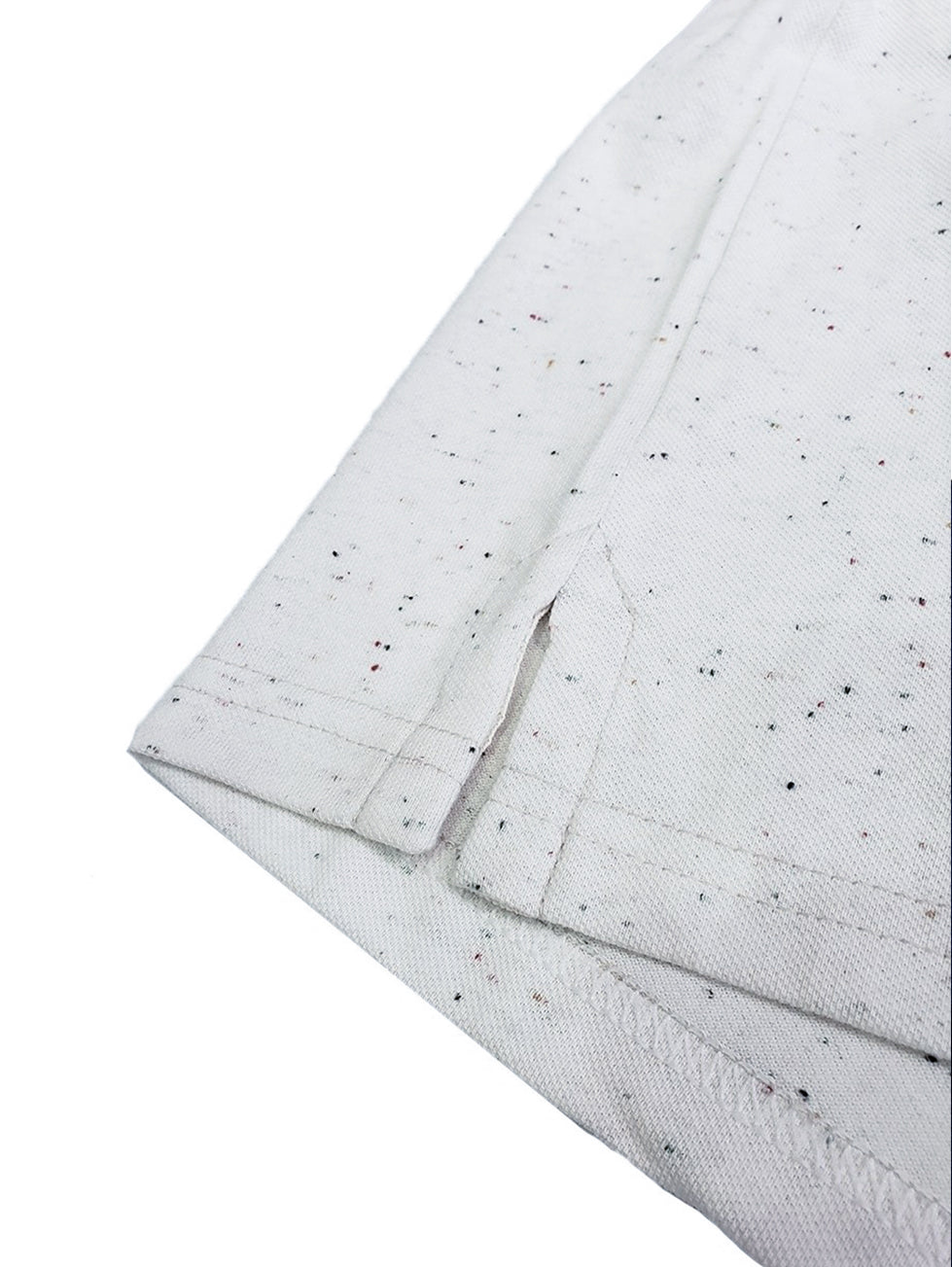 Primer plano del acabado inferior de un polo Dubrovnik gris claro jaspeado, mostrando la abertura lateral con refuerzo y la textura de moteado multicolor