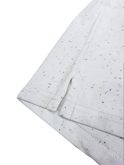 Primer plano del acabado inferior de un polo Dubrovnik gris claro jaspeado, mostrando la abertura lateral con refuerzo y la textura de moteado multicolor