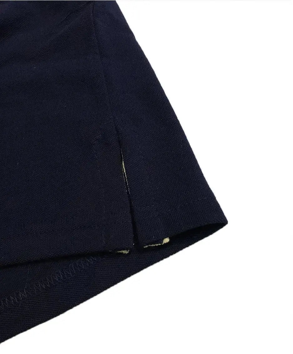 Primer plano del acabado inferior de un polo Dubrovnik negro, mostrando la abertura lateral con cinta de refuerzo interna en color blanco y doble costura de seguridad