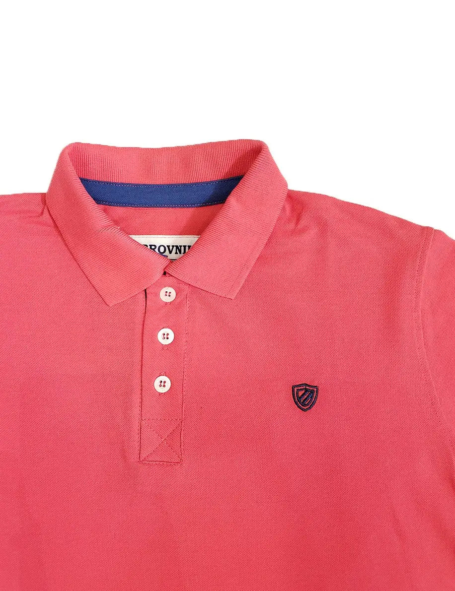 Primer plano de polo Dubrovnik color coral, mostrando la carterita interna en azul marino, botones blancos perlados y el escudo bordado de alta densidad en el pecho