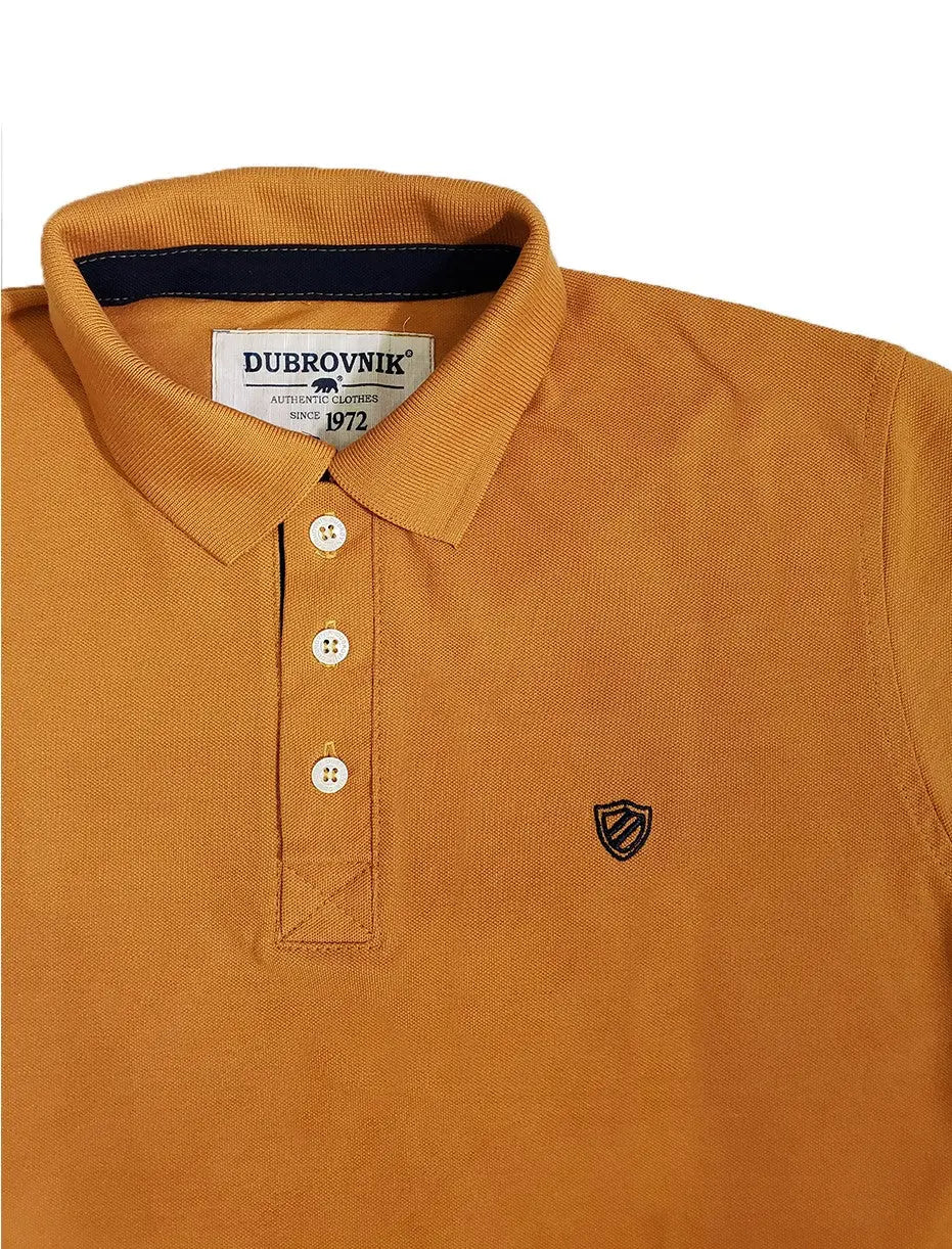 Primer plano de polo Dubrovnik color mostaza, mostrando el contraste azul marino en el cuello interno, botones blancos reforzados y el escudo bordado con alta definición