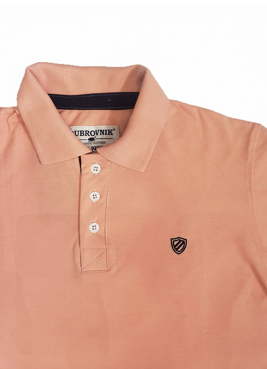 Primer plano de polo Dubrovnik color salmón, mostrando el contraste azul marino en el cuello interno, botones blancos reforzados y el escudo bordado con precisión técnica