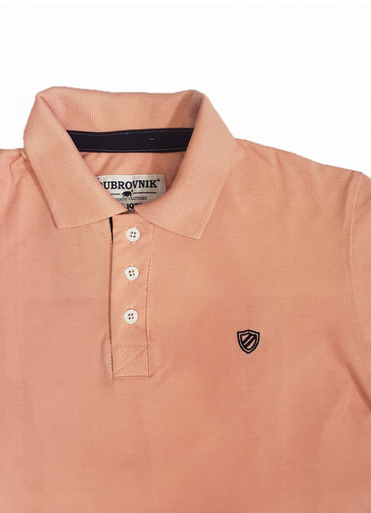 Primer plano de polo Dubrovnik color salmón, mostrando el contraste azul marino en el cuello interno, botones blancos reforzados y el escudo bordado con precisión técnica