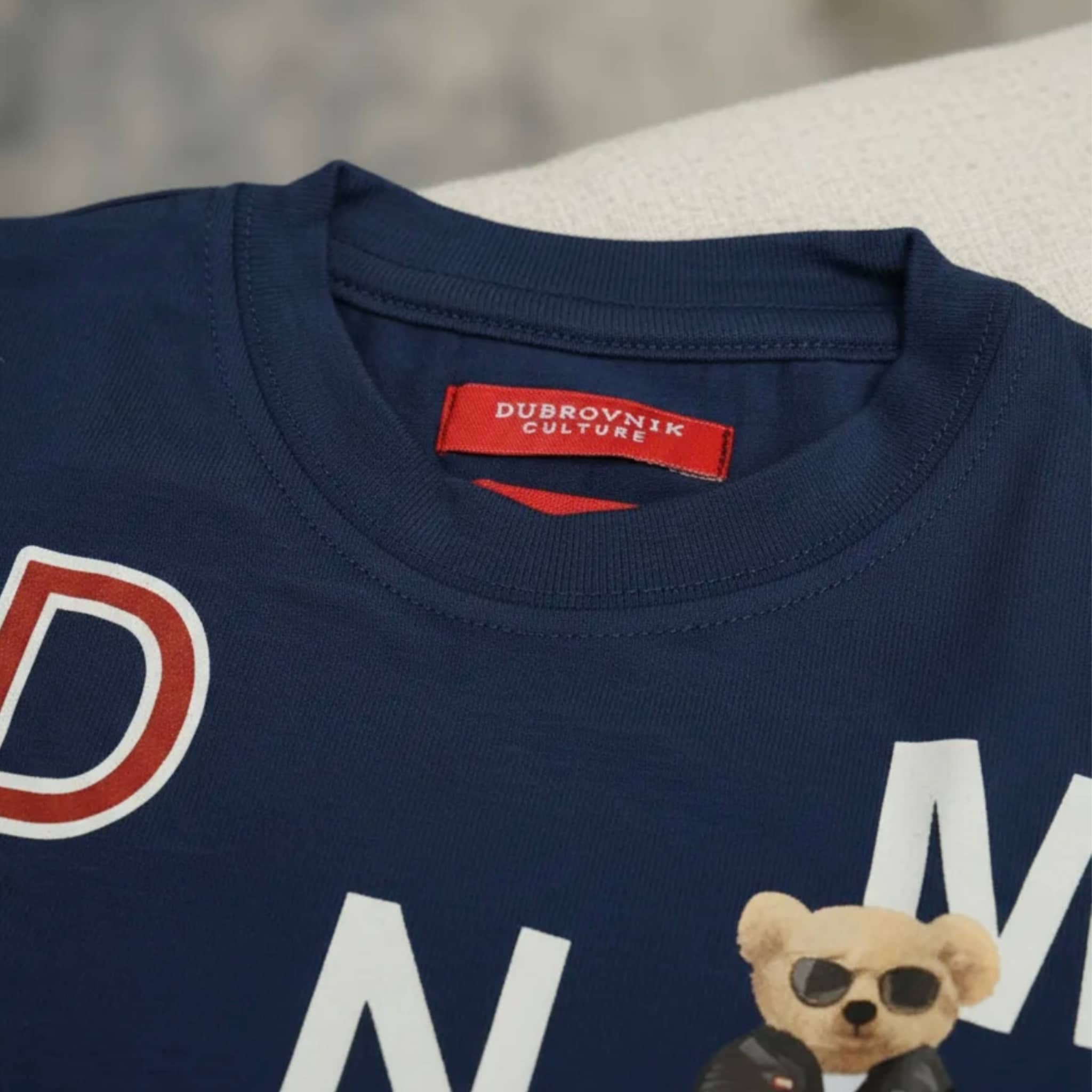 Primer plano del cuello de una camiseta azul marino para niño con etiqueta roja Dubrovnik Culture y estampado gráfico