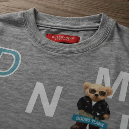 Primer plano del cuello de una camiseta gris jaspeada para niño con etiqueta roja "Dubrovnik Couture" y estampado de oso con gafas