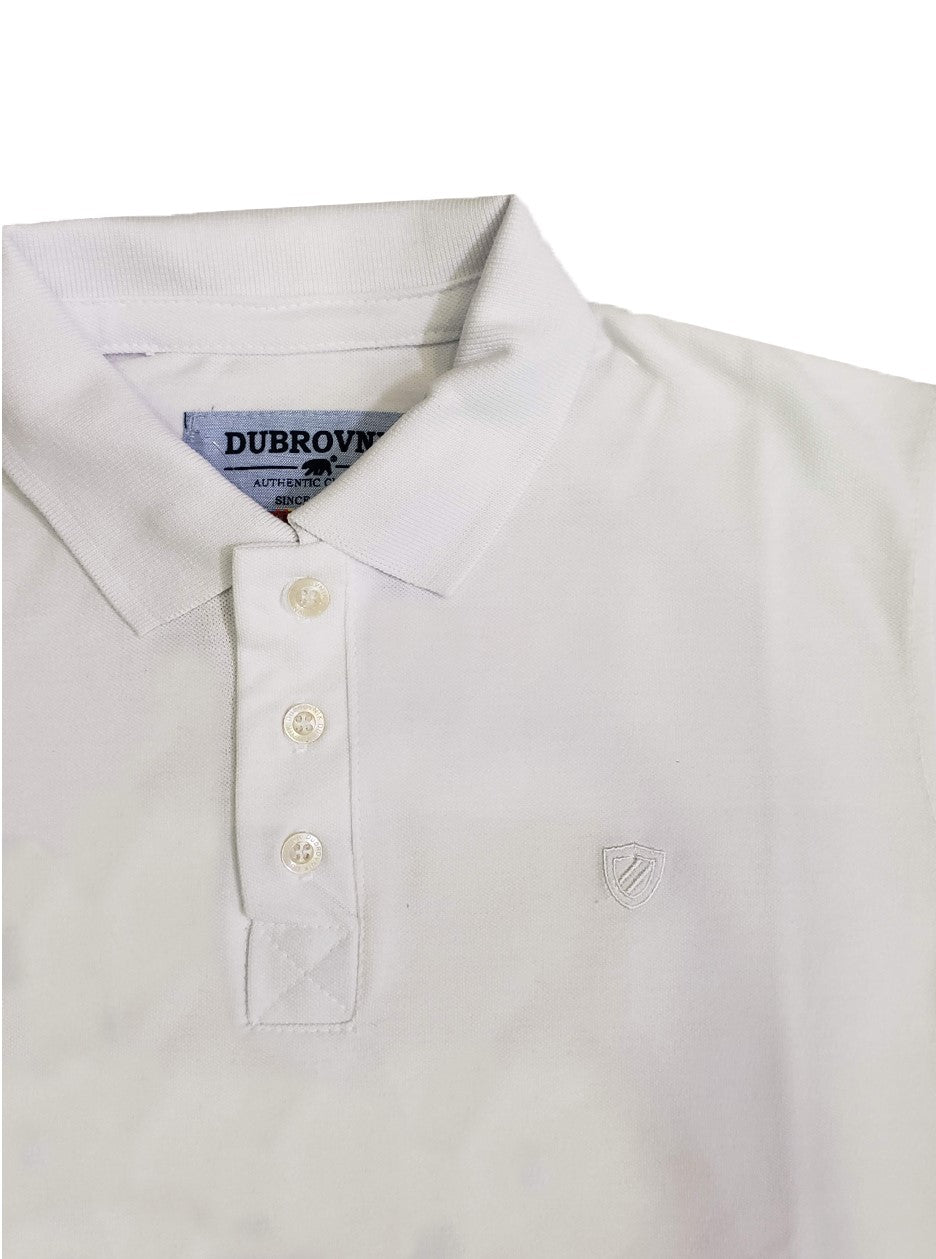 Primer plano del cuello de un polo infantil blanco de la marca Dubrovnik, mostrando la carterita con tres botones, la etiqueta de la marca y el escudo bordado a tono en el pecho sobre tejido piqué