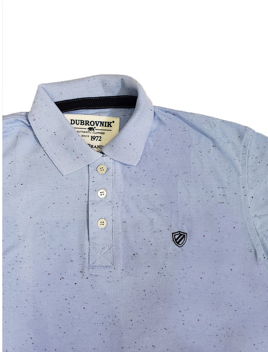 Primer plano del cuello de un polo infantil celeste jaspeado con micro-estampado, mostrando el ribete interno azul marino, la etiqueta clásica de Dubrovnik y el escudo bordado en gris oscuro