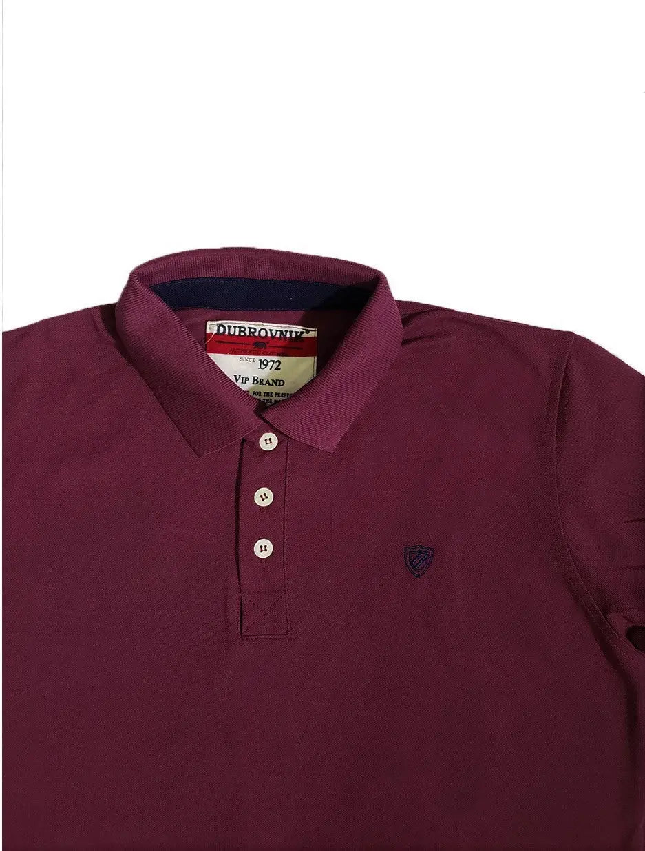 Primer plano del cuello de un polo color ciruela de la marca Dubrovnik, mostrando la etiqueta "Since 1972", la botonera con botones blancos y el pequeño escudo bordado en azul marino en el pecho