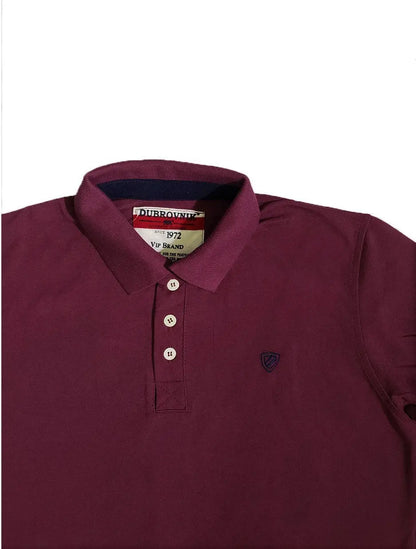 Primer plano del cuello de un polo color ciruela de la marca Dubrovnik, mostrando la etiqueta "Since 1972", la botonera con botones blancos y el pequeño escudo bordado en azul marino en el pecho