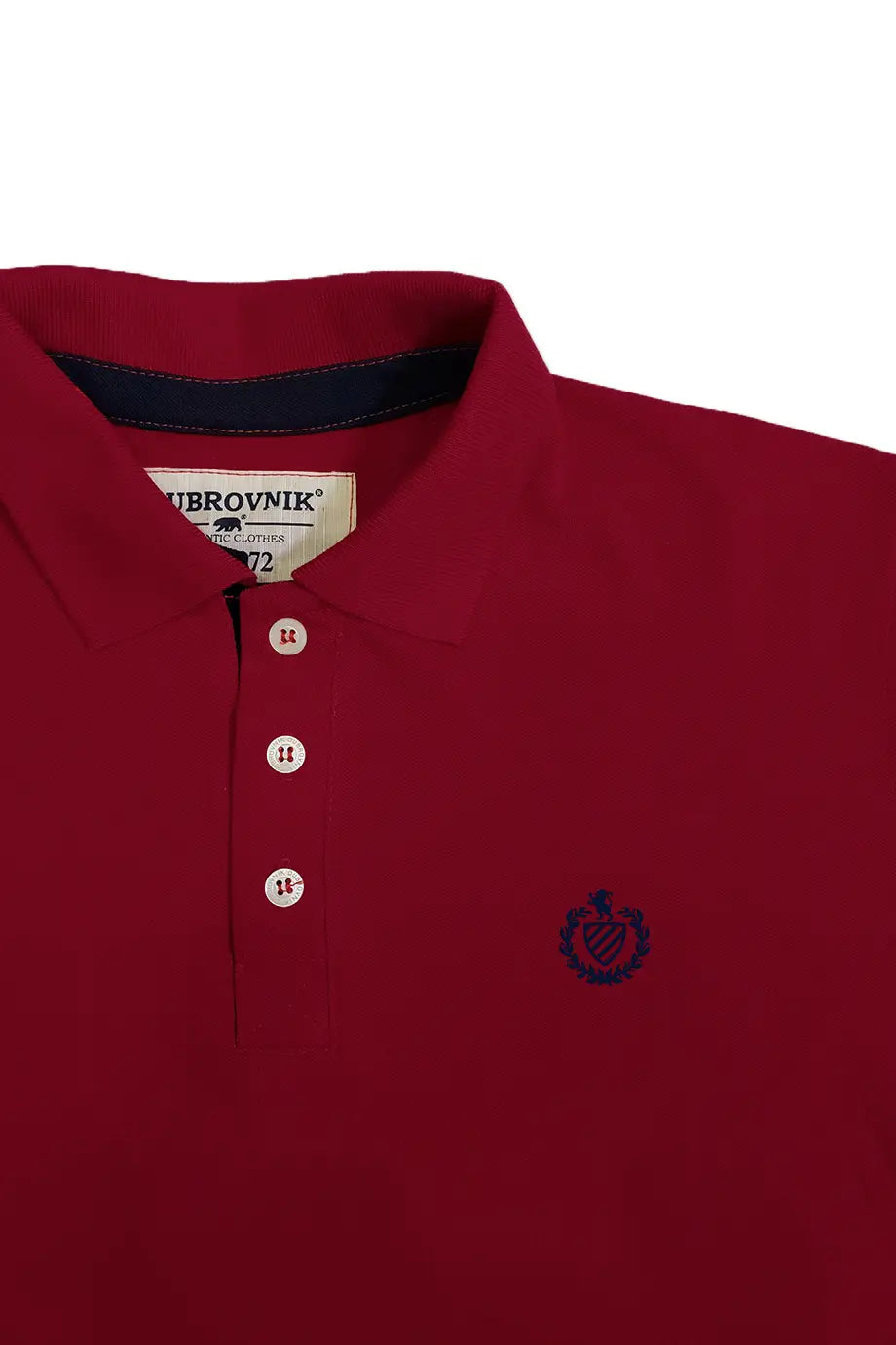 Primer plano del cuello de un polo color granate de la marca Dubrovnik, mostrando la etiqueta interna, la botonera con tres botones blancos y el logotipo bordado de un escudo con un león en el pecho