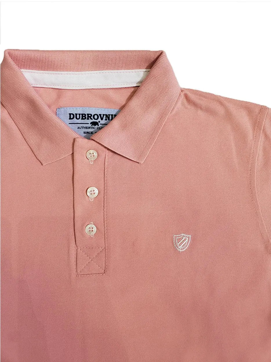 Primer plano del cuello de un polo infantil en color rosa pastel de la marca Dubrovnik, mostrando la cinta interna en color blanco, tres botones claros y el logotipo de escudo bordado en hilo blanco sobre el pecho