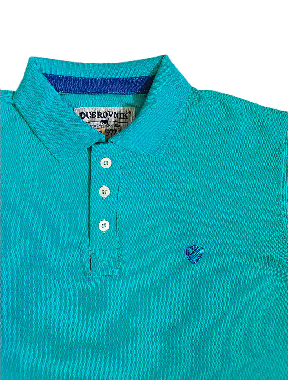 Primer plano del cuello de un polo color turquesa de la marca Dubrovnik, mostrando la etiqueta interna, la botonera con botones blancos y el pequeño logotipo de escudo bordado en el pecho