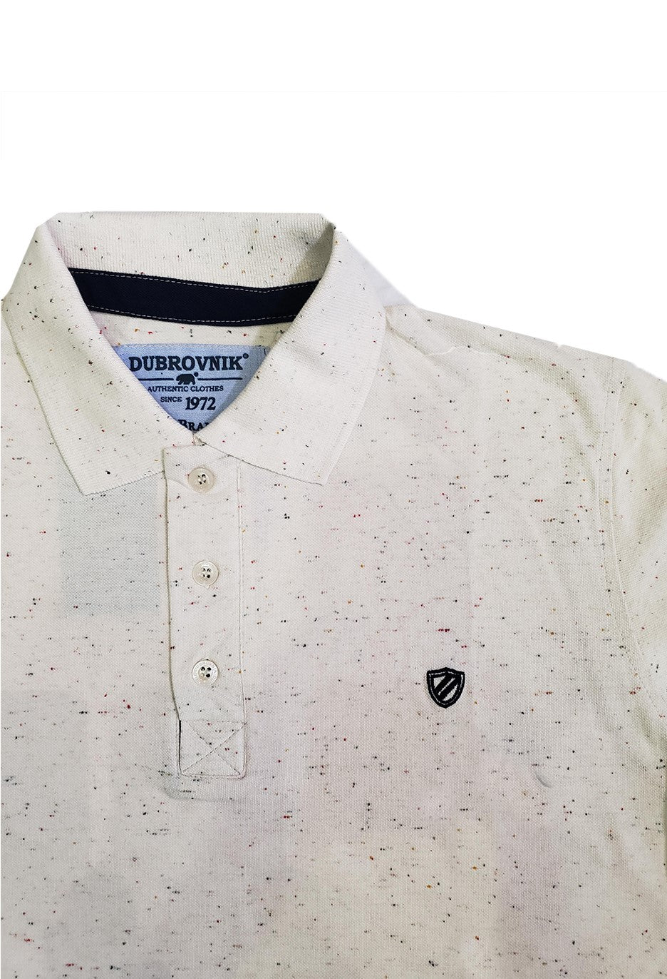 Primer plano de polo Dubrovnik beige con efecto jaspeado multicolor, destacando la cinta interna en azul marino, botones perlados y el escudo bordado en contraste