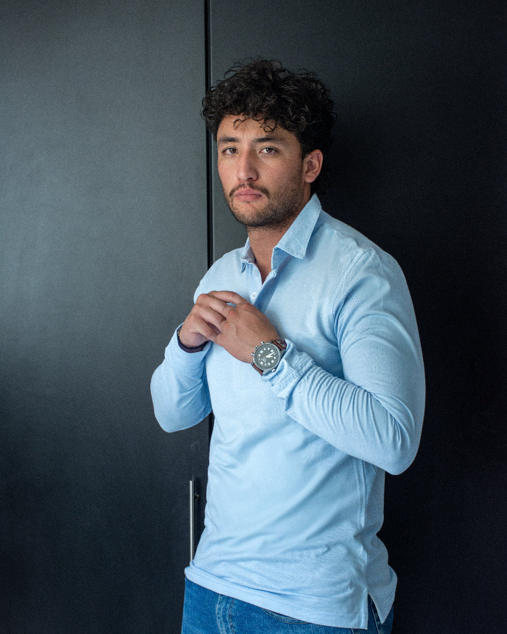 Primer plano de hombre con polo de manga larga celeste claro, destacando el diseño del cuello camisero y los botones a tono