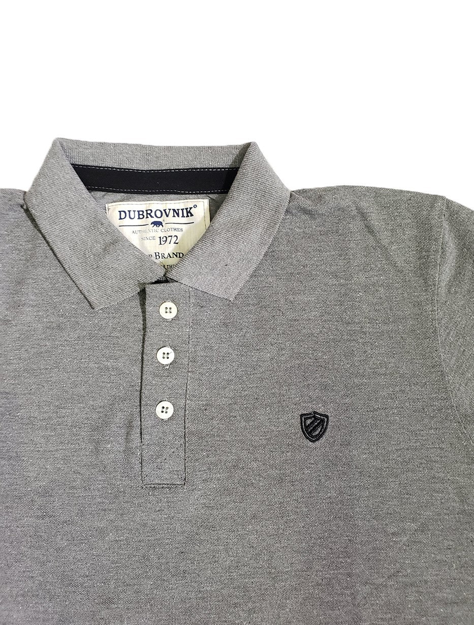 Primer plano de polo Dubrovnik color gris oxford, resaltando la cinta de refuerzo negra en el cuello, botones blancos perlados y el escudo bordado tipo blasón