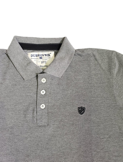 Primer plano de polo Dubrovnik color gris oxford, resaltando la cinta de refuerzo negra en el cuello, botones blancos perlados y el escudo bordado tipo blasón