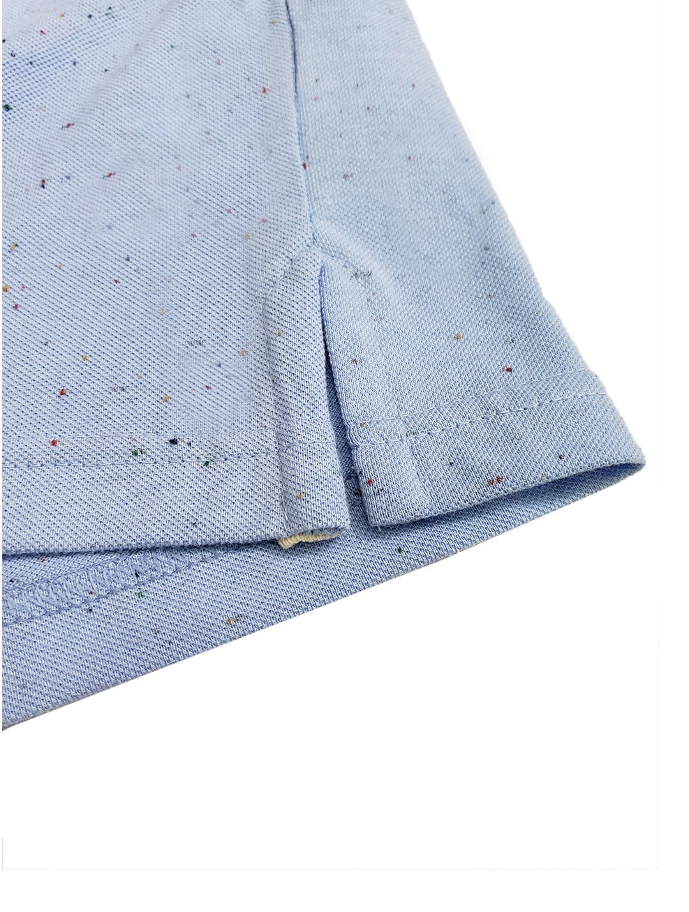 Primer plano del dobladillo inferior de un polo Dubrovnik azul cielo con efecto jaspeado, mostrando la abertura lateral reforzada y la textura del tejido de piqué