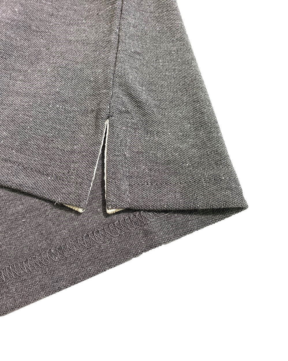 Primer plano del dobladillo inferior de un polo Dubrovnik gris oxford, mostrando la abertura lateral con cinta de refuerzo interna clara y costura de precisión