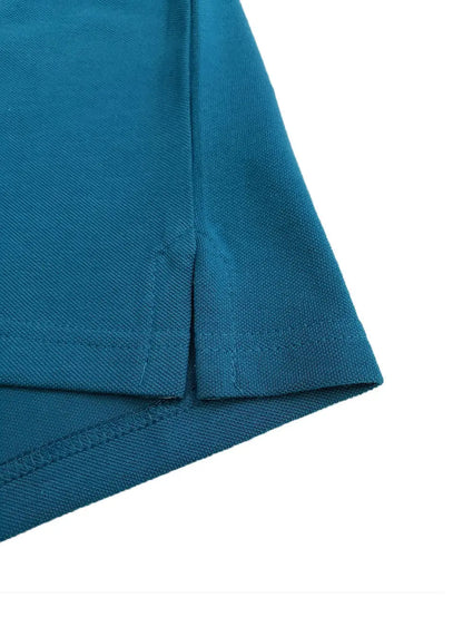 Primer plano del detalle de la costura y la abertura lateral inferior de un polo infantil en color turquesa oscuro, resaltando la calidad del acabado y el tejido piqué de la marca Dubrovnik