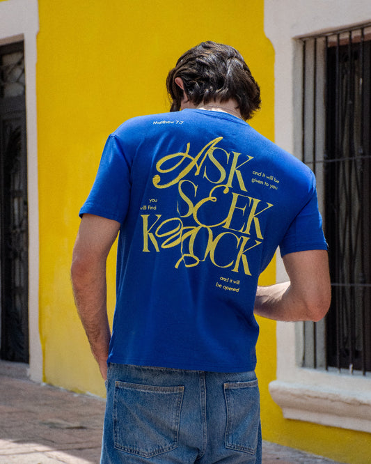 Hombre sonriente sentado en el exterior vistiendo un jersey de manga larga verde agua de textura lineal y firma gráfica en el pecho de la marca Dubrovnik