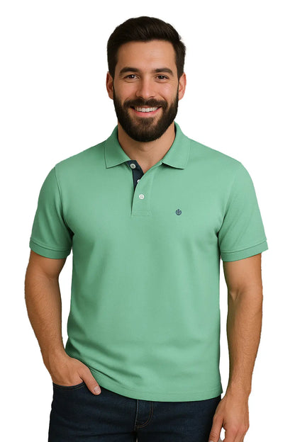 Hombre con barba sonriendo con un polo de manga corta en color verde jade suave, con contraste azul marino en la carterita interna del cuello y logotipo bordado, de la marca Dubrovnik